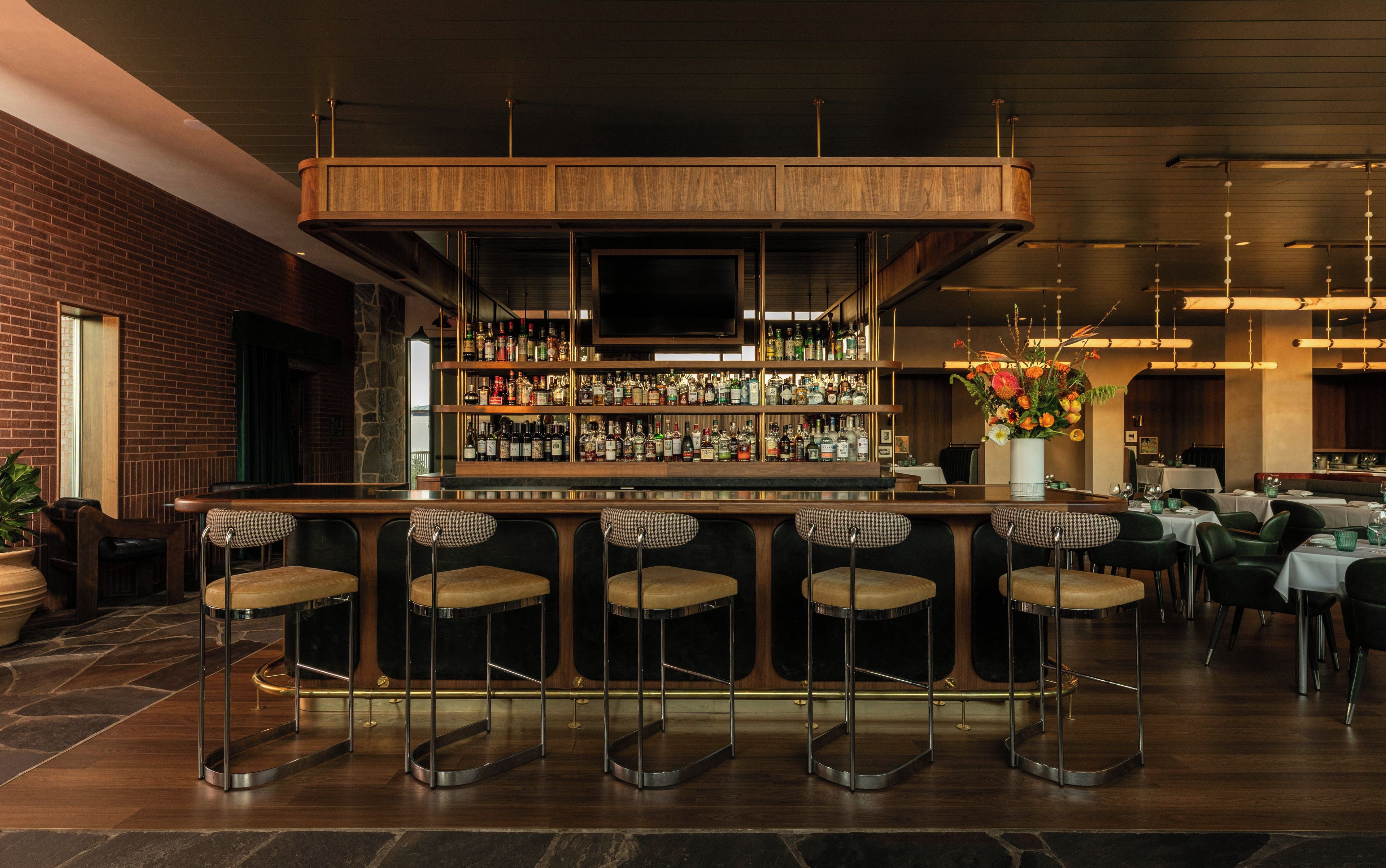 A bar area with a wooden bar counter, multiple stools, and a variety of bottles.