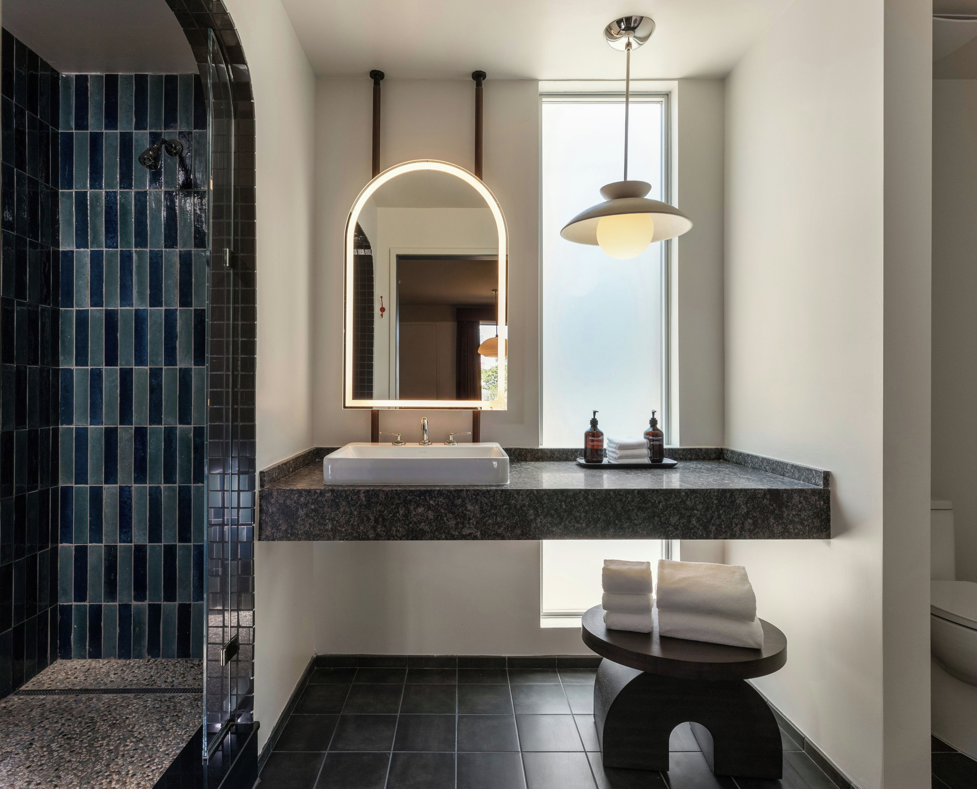 Un baño moderno con lavamanos independiente, un espejo grande y una zona de ducha con azulejos azules.