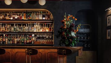 Un bar con piso a cuadros, taburetes de bar, una estantería con botellas de licores y un arreglo floral.