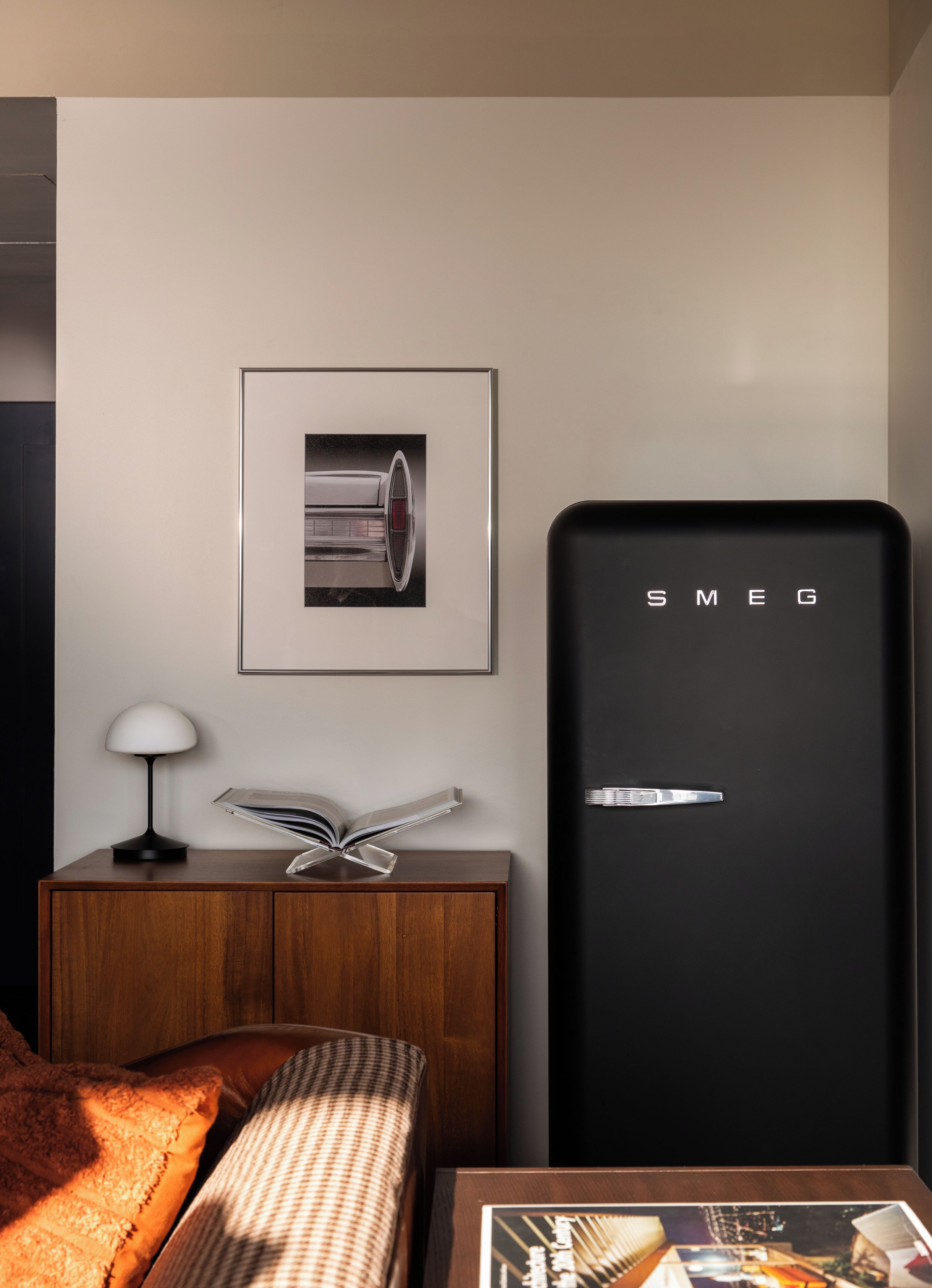 Ein modernes Zimmer mit einem Bett, einem Nachttisch mit Lampe, einem gerahmten Bild und einem schwarzen Kühlschrank mit 'SMEG'.