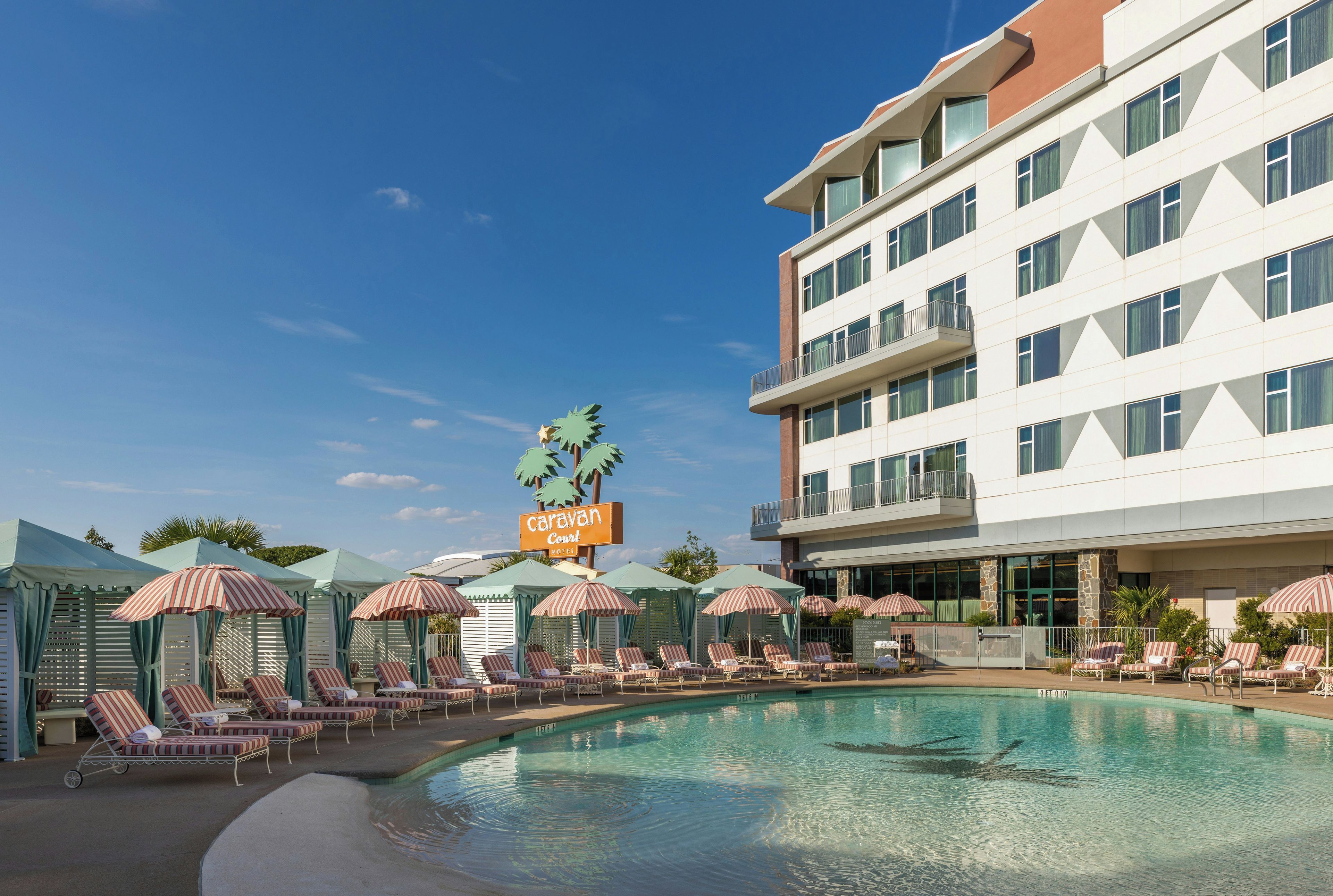 A hotel with a swimming pool, lounge chairs, and umbrellas.
