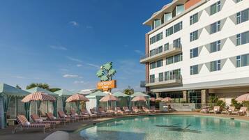 A hotel with a swimming pool, lounge chairs, and umbrellas.