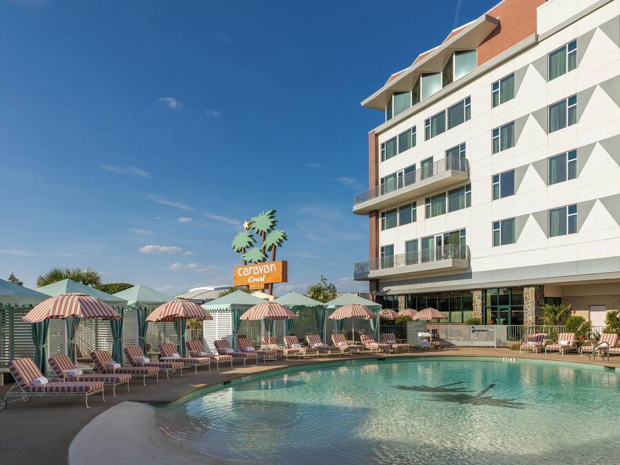 A hotel with a swimming pool, lounge chairs, and umbrellas.