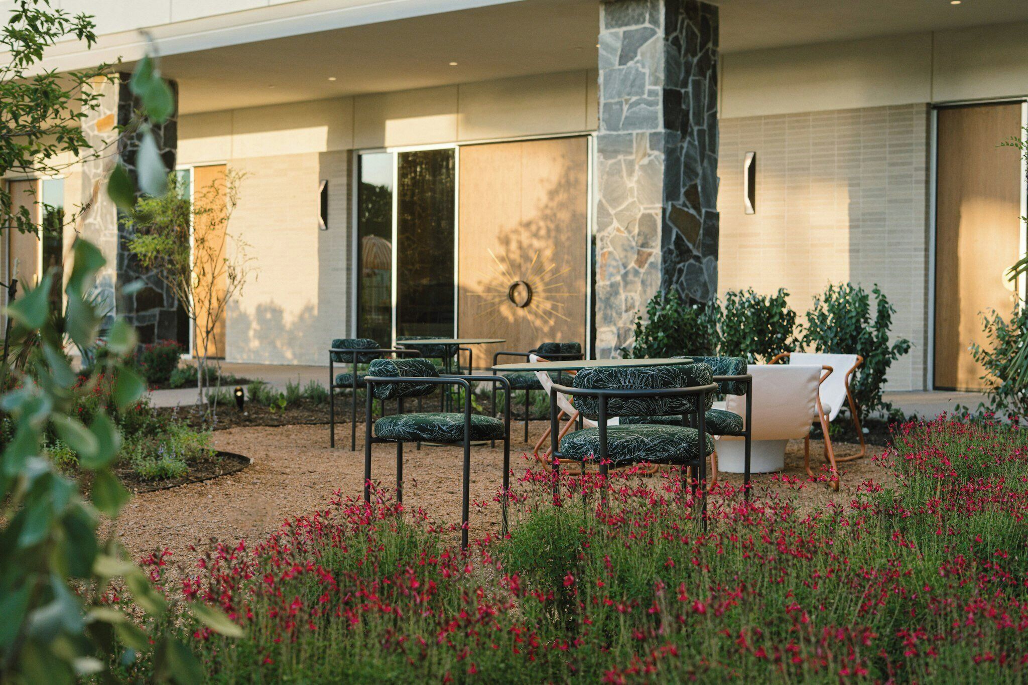 An outdoor seating area with chairs and tables, surrounded by a garden with red flowers.