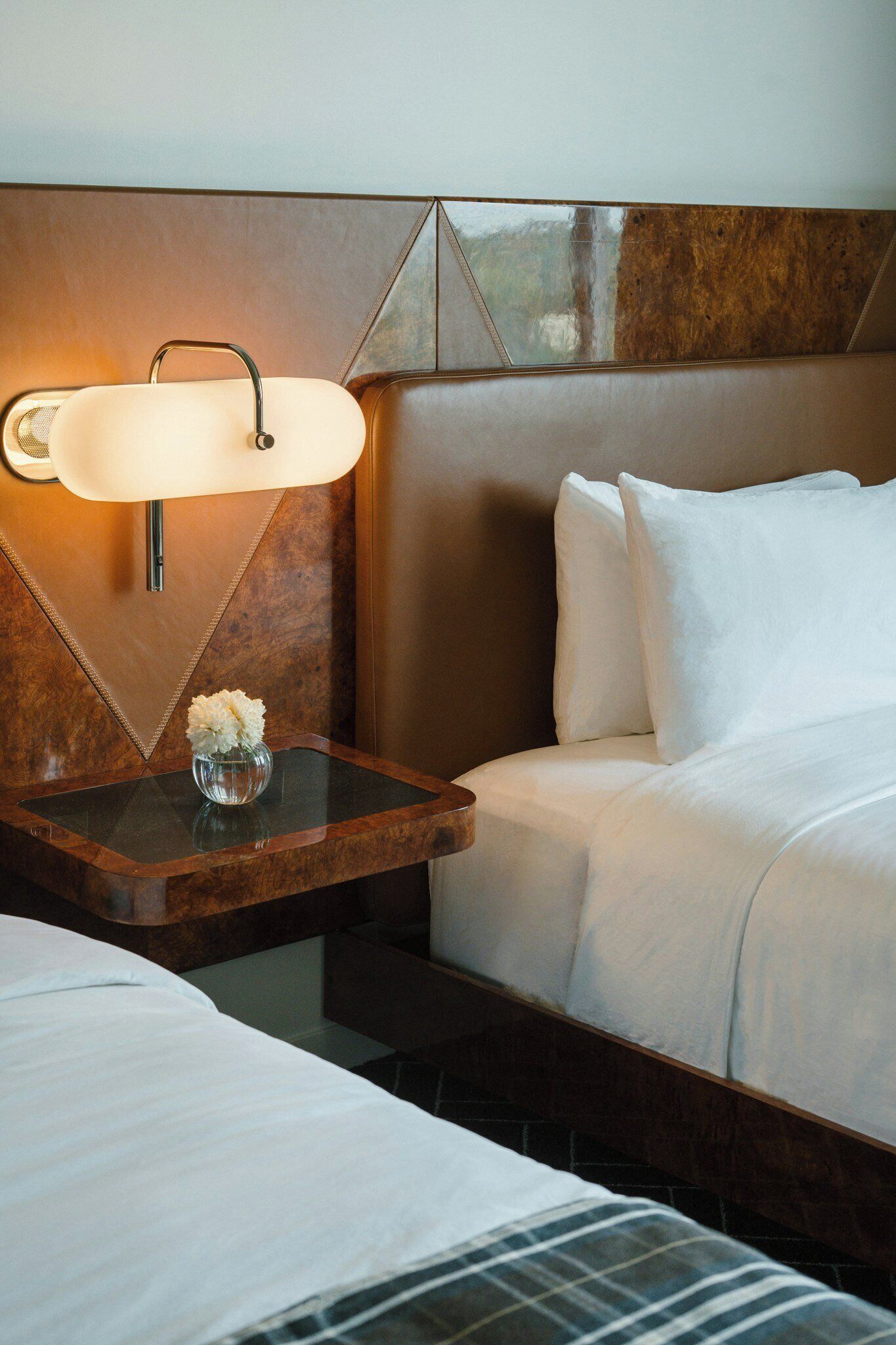 Une chambre d’hôtel avec un lit, une table de chevet avec une lampe et un vase de fleurs.