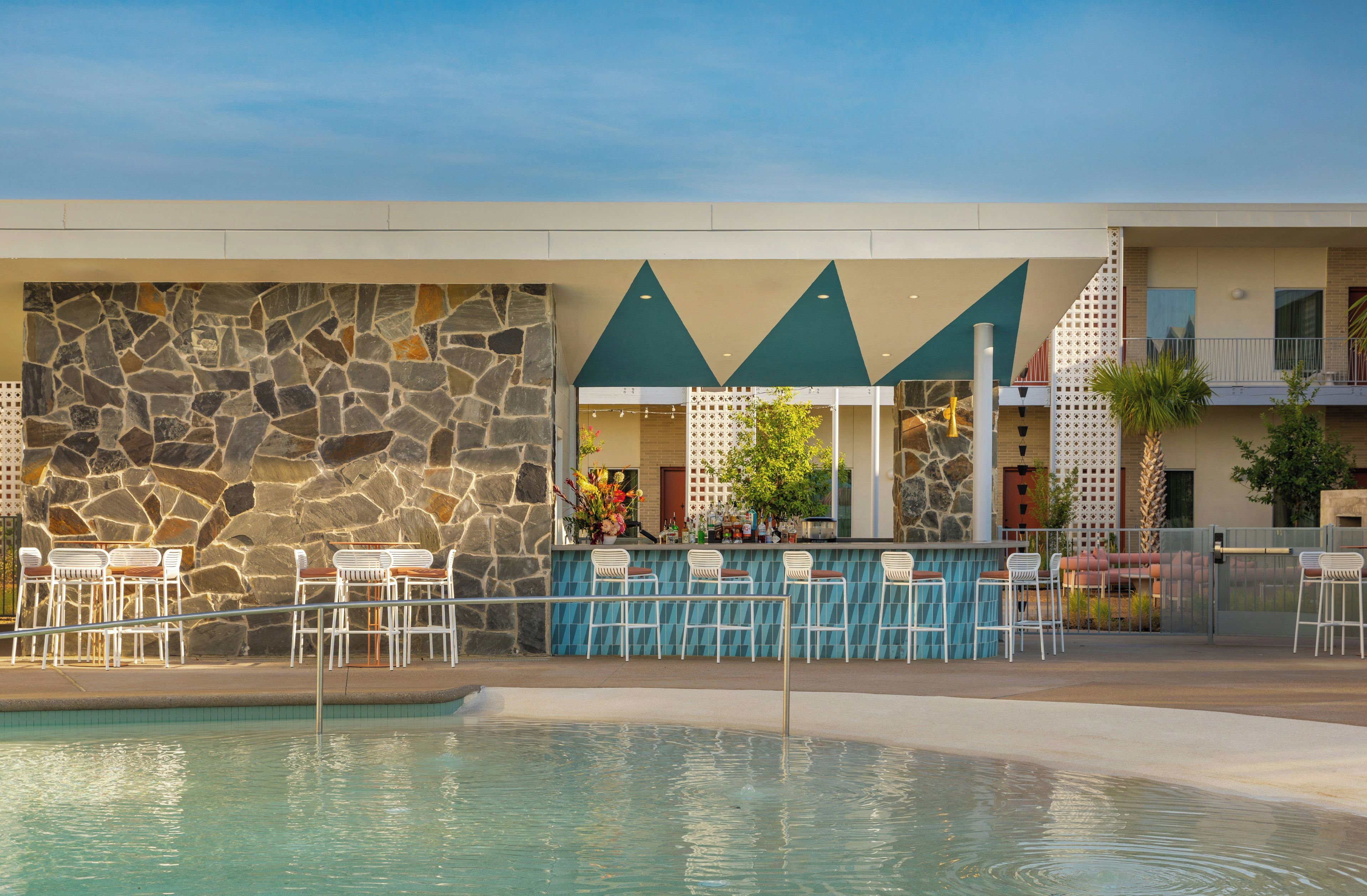 Área de bar junto à piscina, com paredes de pedra, piscina e mesas ao ar livre.