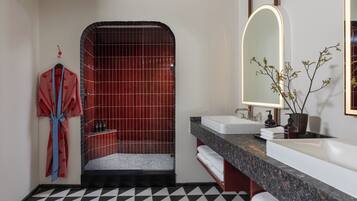 A modern bathroom with a black and white checkered floor, a shower with red tiles, a vanity with a marble countertop, and a mirror with a lighted frame.