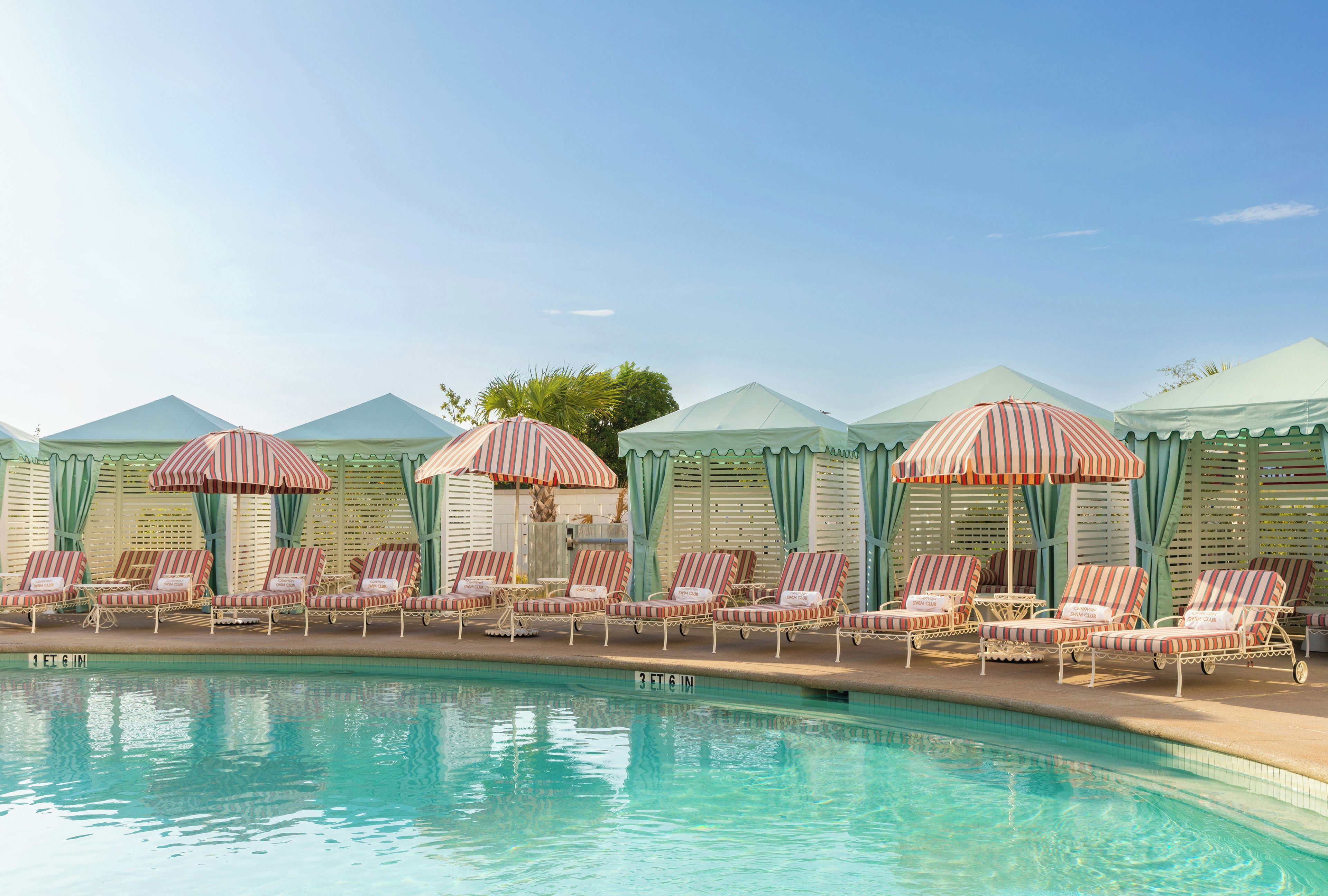 A poolside area with lounge chairs and striped umbrellas, a clear sky, and a pool with visible lane markers.