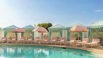 A poolside area with lounge chairs and striped umbrellas, a clear sky, and a pool with visible lane markers.