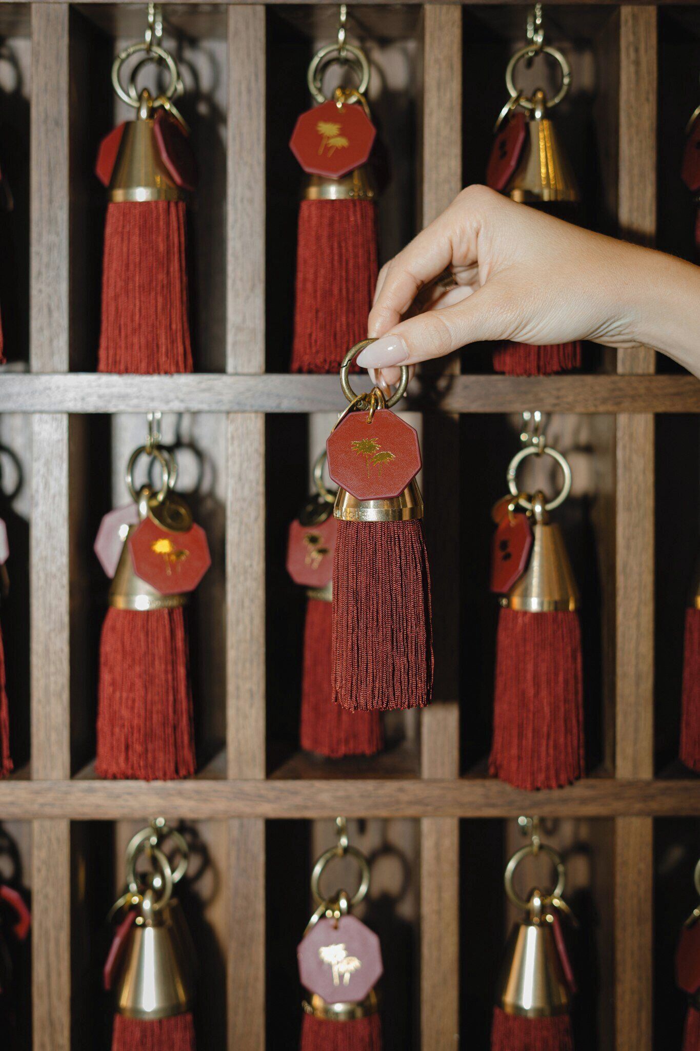 A hand selecting a keychain with a tassel from a wooden shelf.