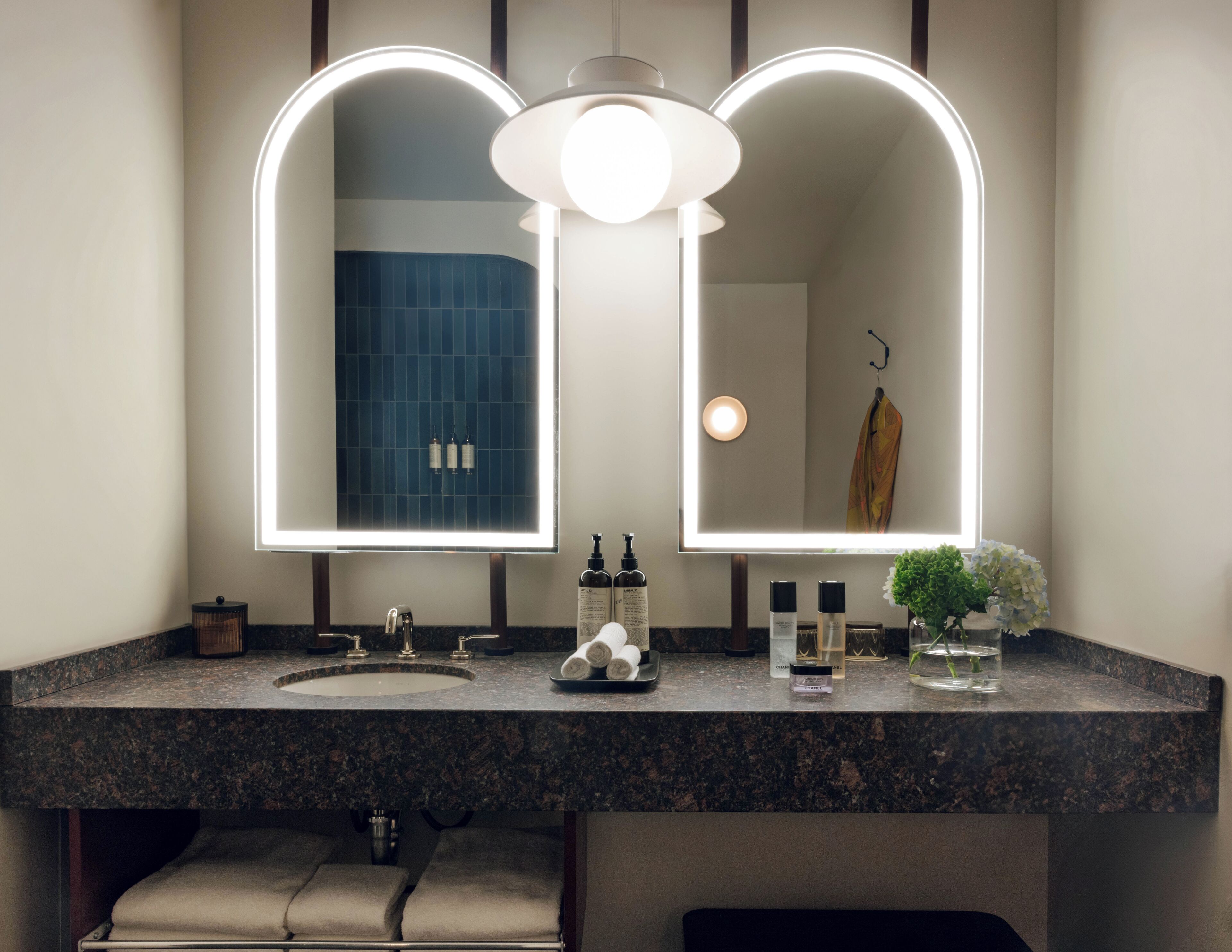 Un baño con lavamanos doble, un espejo grande con iluminación integrada, un lavabo y una planta pequeña en la encimera.