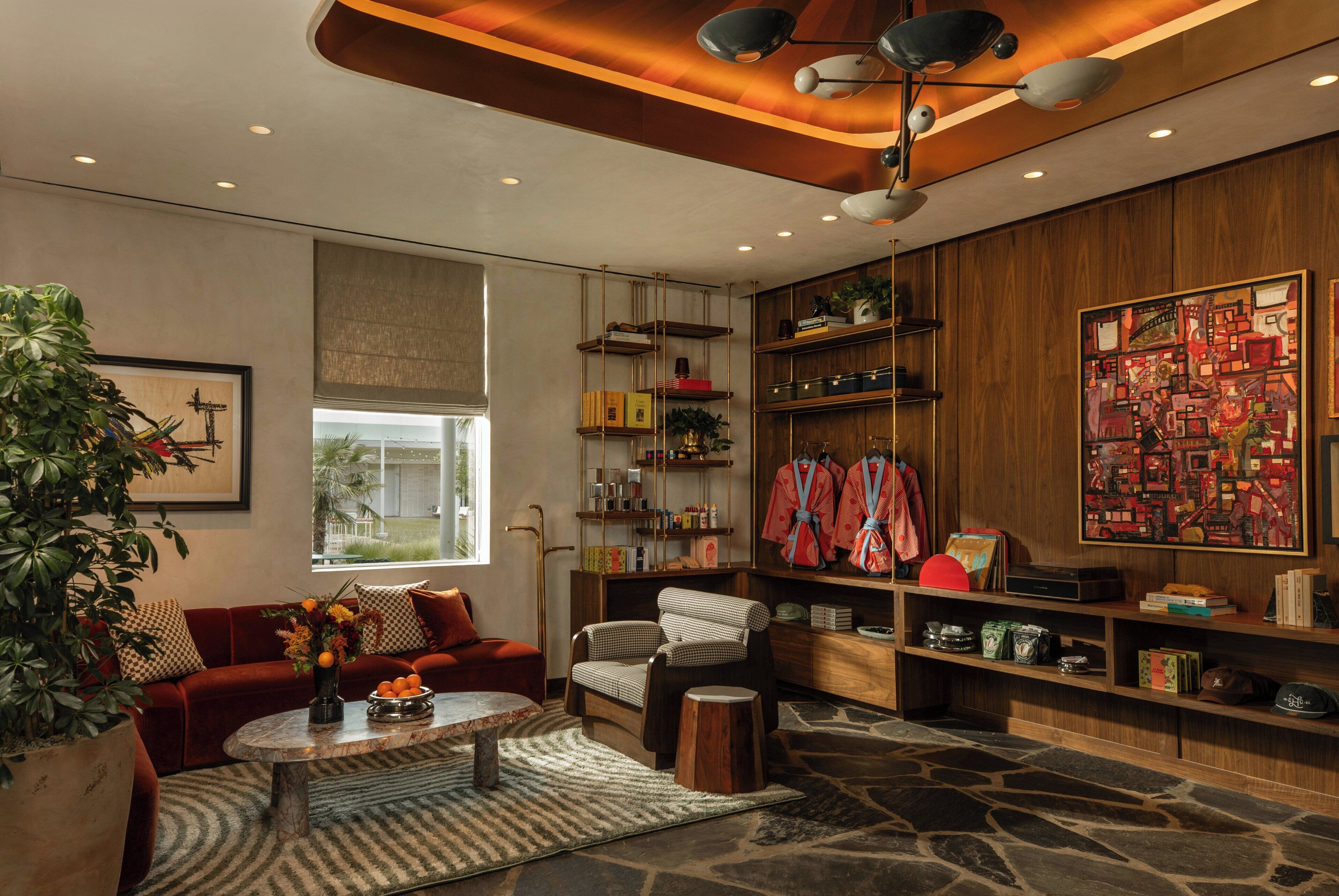 Un salon moderne avec un sol en pierre, un canapé rouge, un fauteuil à carreaux, une table basse et une bibliothèque remplie de livres et d’objets décoratifs.