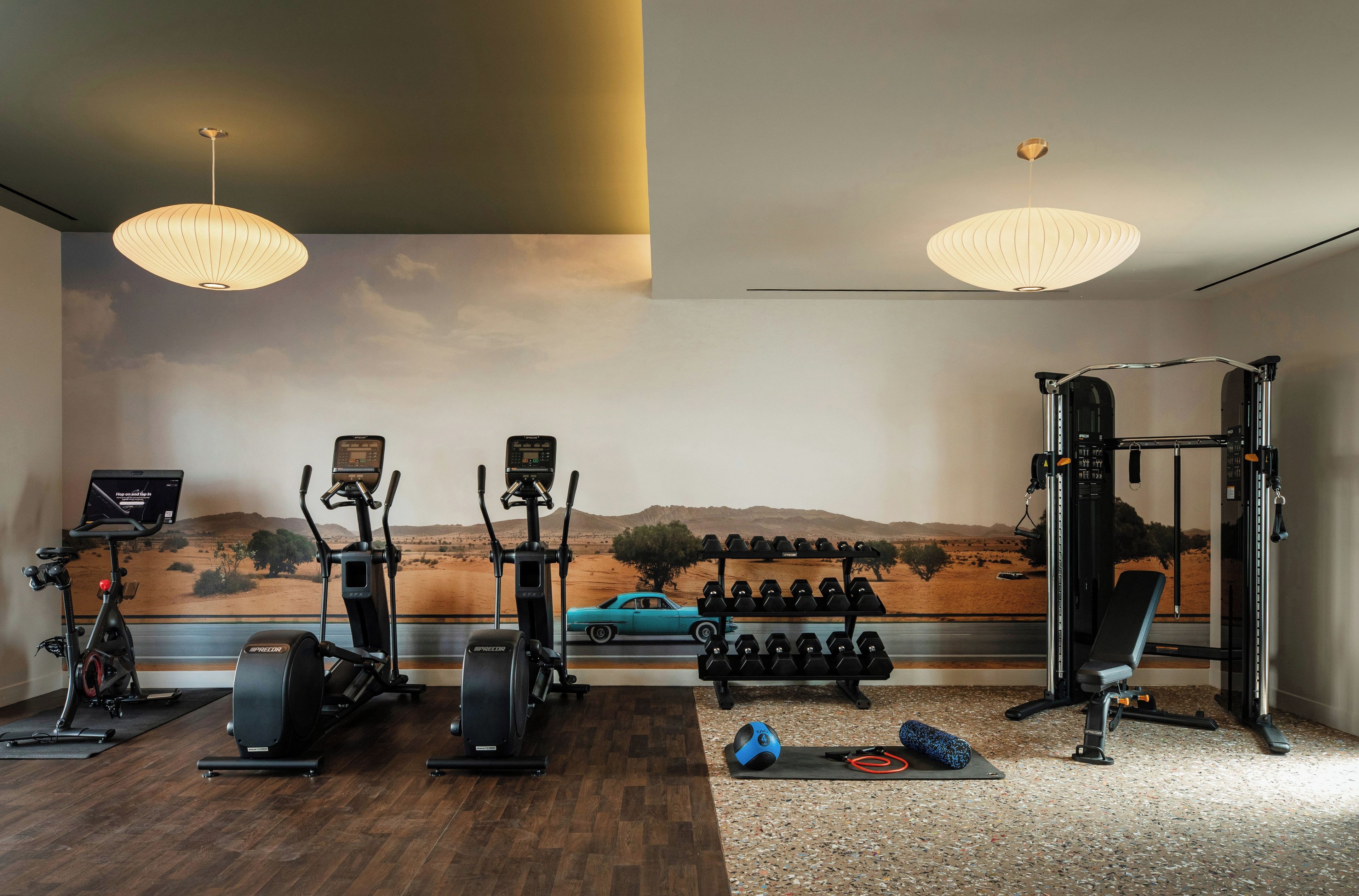 Un gimnasio en casa con equipo de ejercicio, un mural en la pared y un modelo de coche.