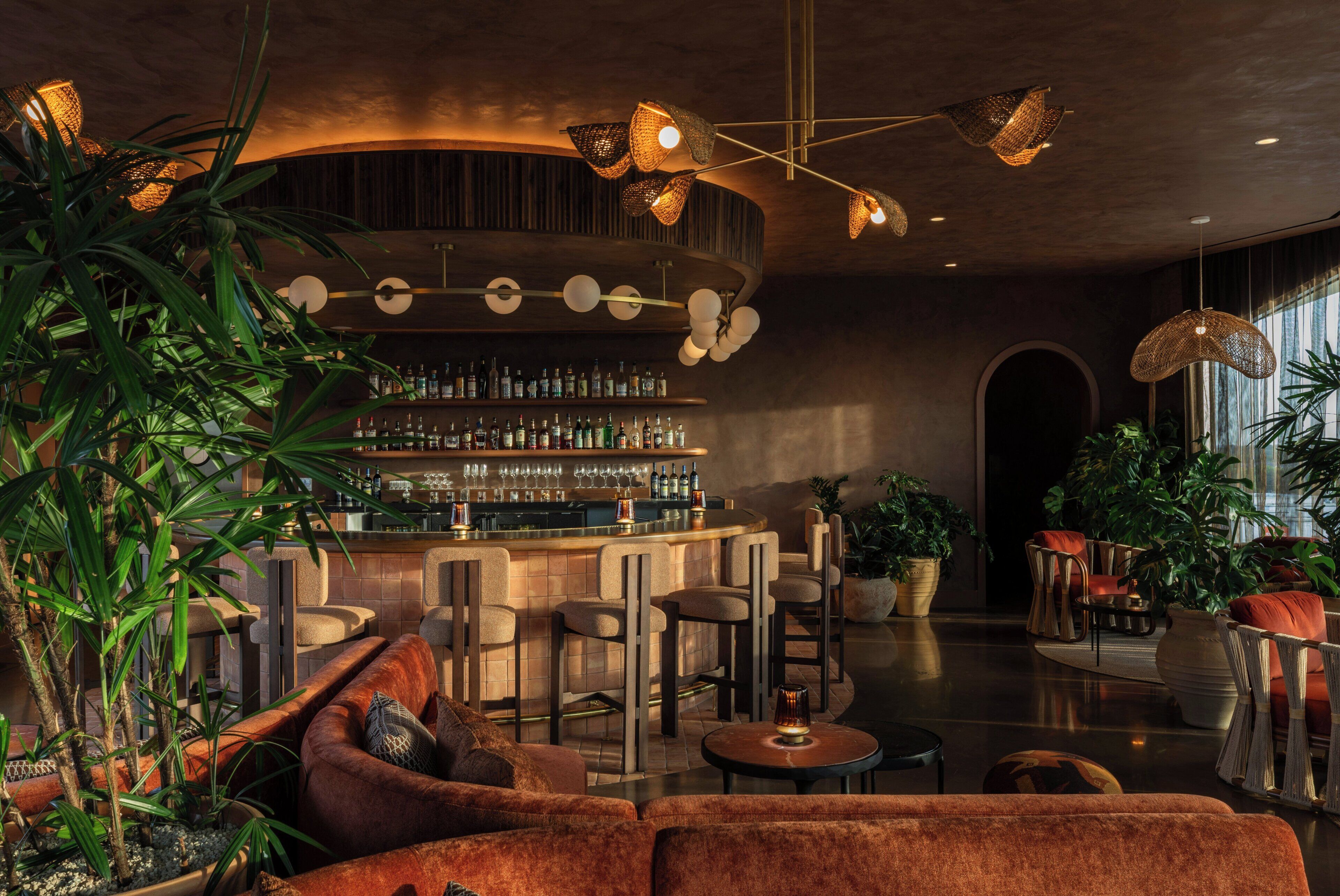 Un espace bar doté d’un comptoir incurvé, de plusieurs options d’assises, notamment un canapé et des fauteuils, et d’une variété de plantes.