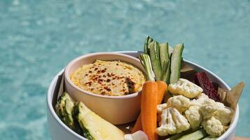 Un bol rempli de nourriture, avec des légumes et une sauce, placé au-dessus d’une piscine.