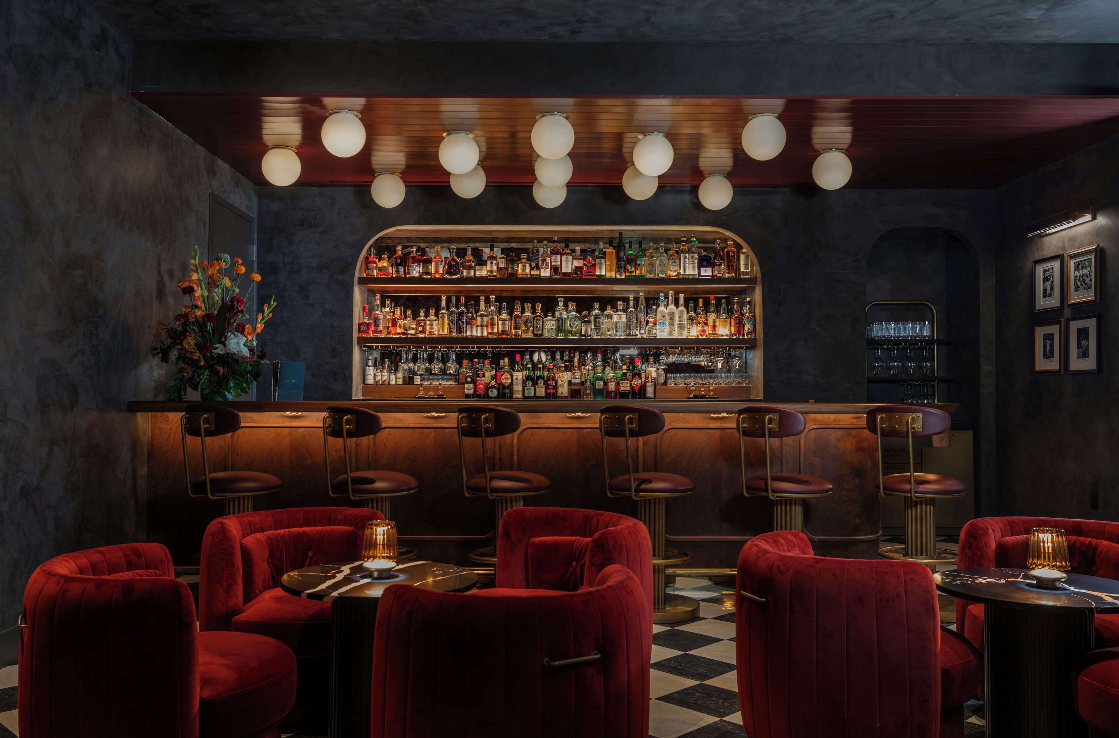 Zona de bar con diversas opciones de asientos, una estantería repleta de licores y un piso con diseño a cuadros.
