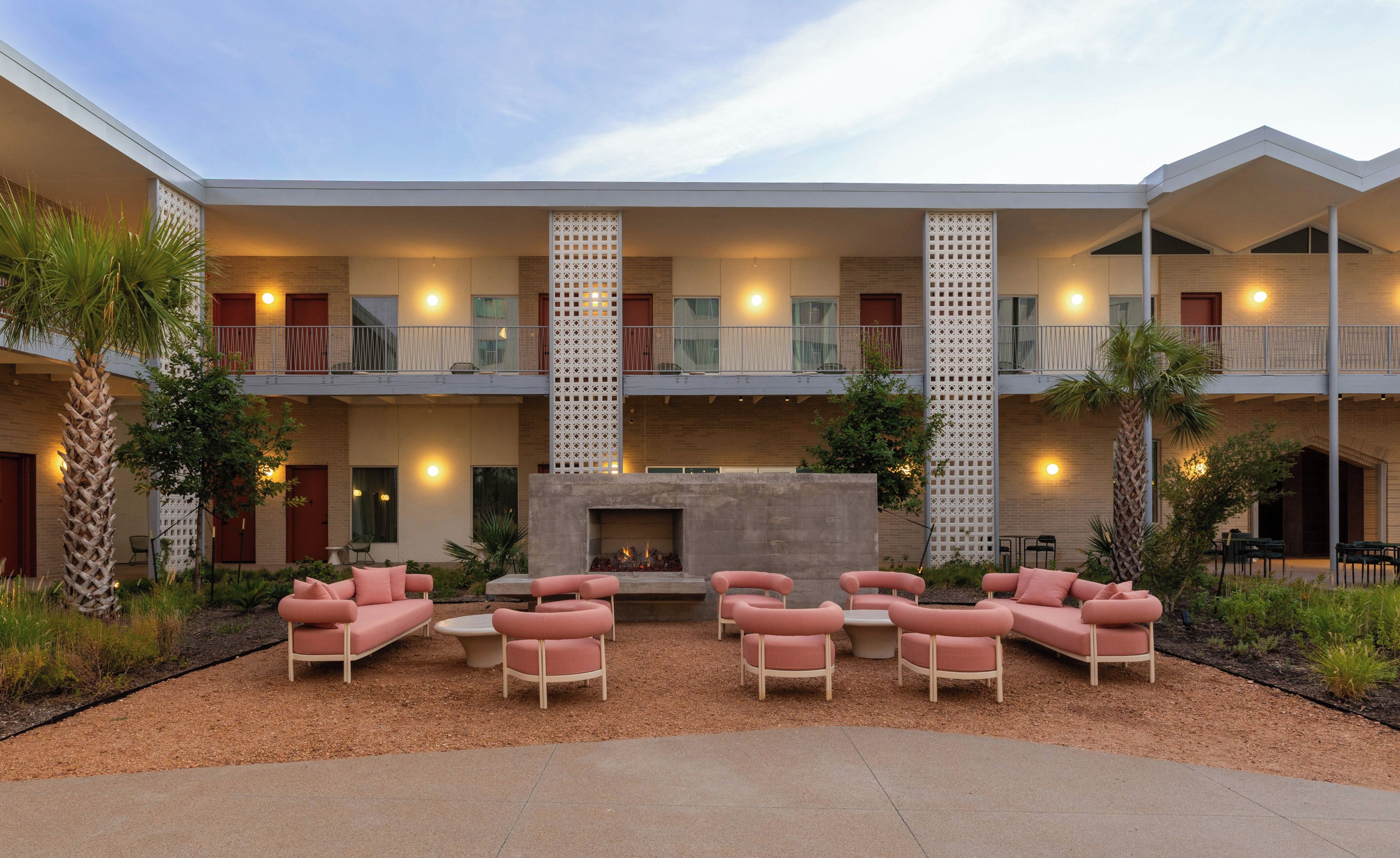 Un hotel con patio central que cuenta con mobiliario exterior, chimenea y varios balcones.
