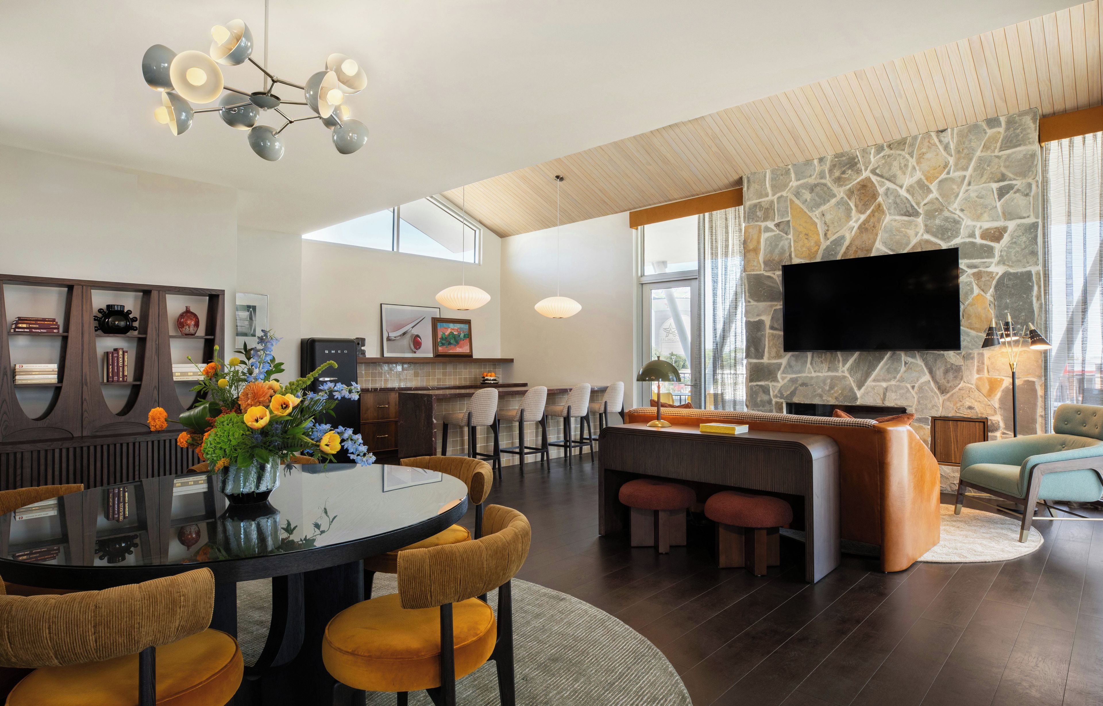 A modern living room with a stone fireplace, a flat-screen TV mounted on the wall, and a dining area with a round table and chairs.