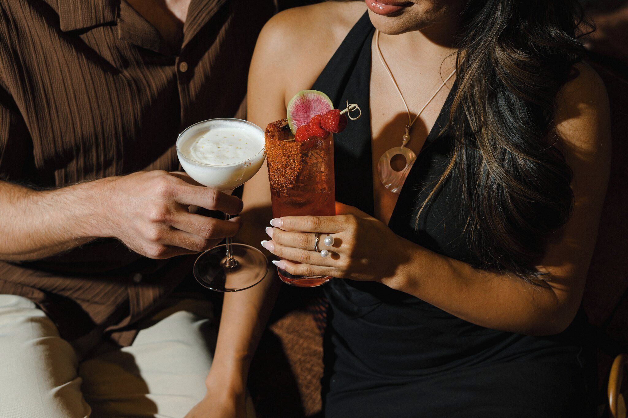 A person holding a cocktail with a garnish and a creamy drink in a glass.