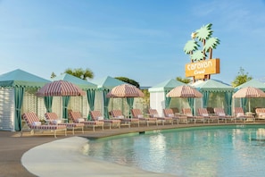 A pool area with lounge chairs and striped umbrellas, a sign for 'Caravan Court Hotel', and palm trees. - Caravan Court, Valencia Collection (Arlington)