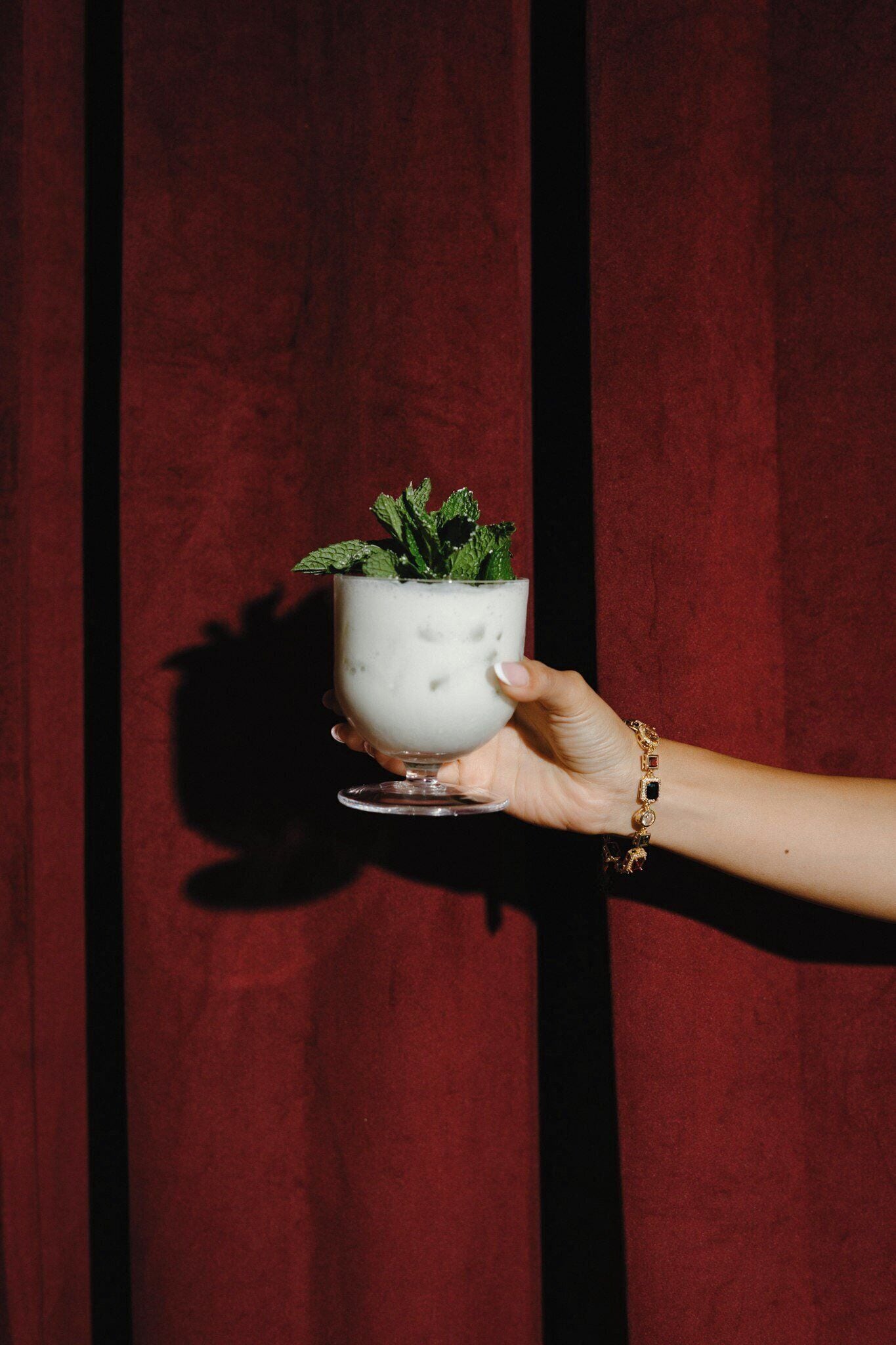 Una mano sostiene una taza blanca con una planta sobre un fondo rojo.