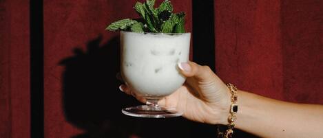 Una mano sostiene una taza blanca con una planta sobre un fondo rojo.