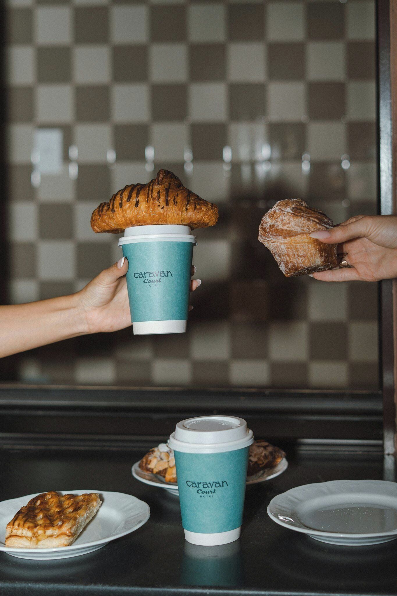 A person holding a croissant and a coffee cup with 'Caravan Hotel' branding.