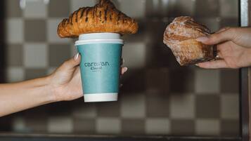 A person holding a croissant and a coffee cup with 'Caravan Hotel' branding.