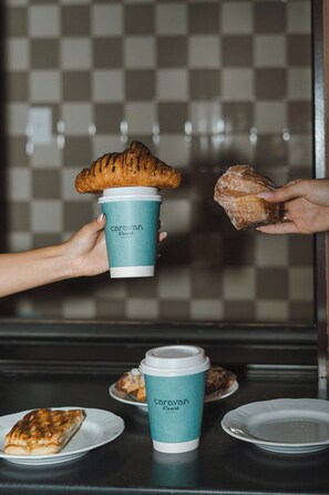 A person holding a croissant and a coffee cup with 'Caravan Hotel' branding. - Caravan Court Hotel (Arlington)