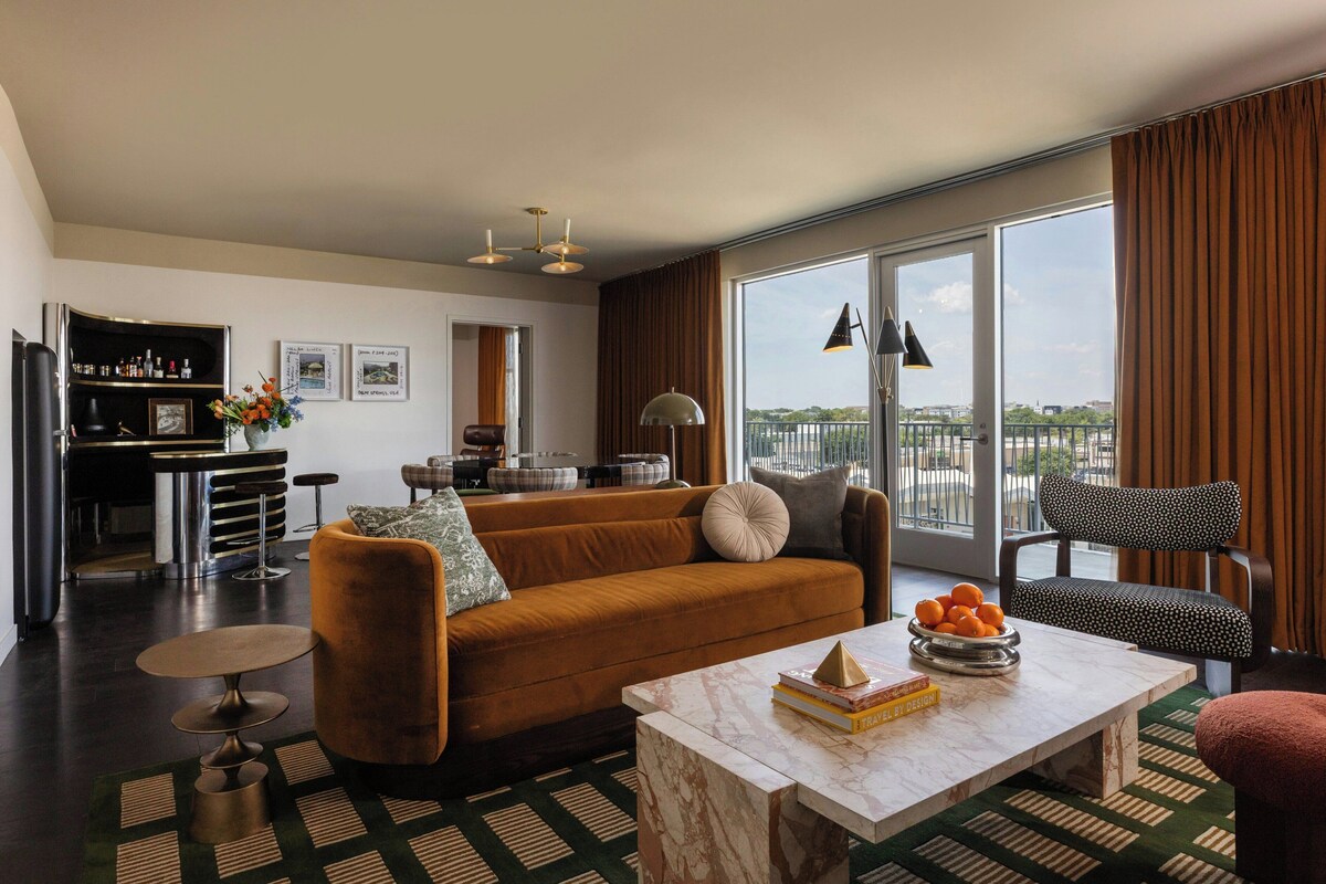 A modern living room with a sofa, coffee table, and a view of the city through large windows.
