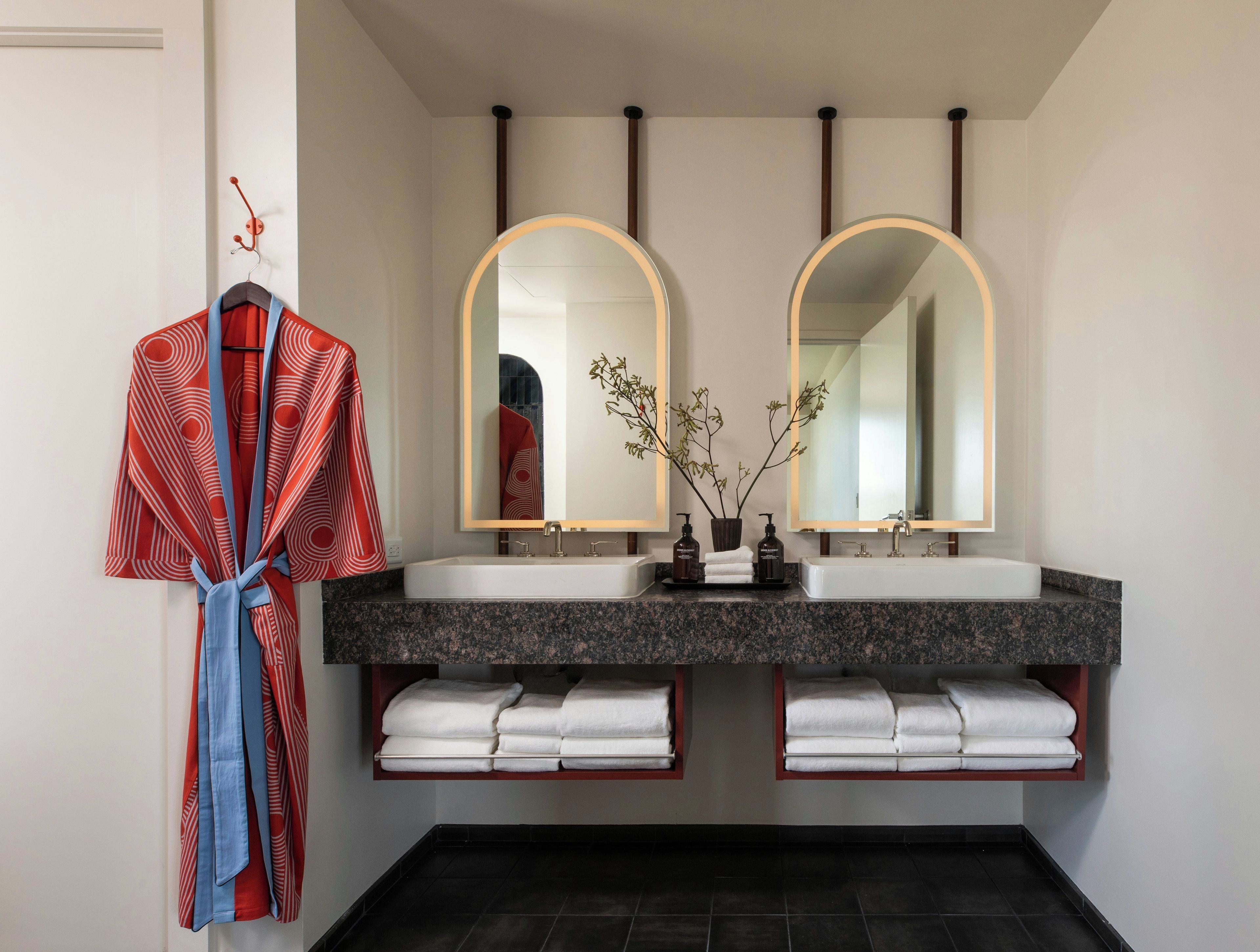 A bathroom with a double sink vanity, a robe hanging on a rack, and a mirror with a circular frame.