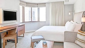 Ein Hotelzimmer mit einem Bett, einem Schreibtisch mit Stuhl, einem Fernseher und einem Fenster mit Vorhängen.