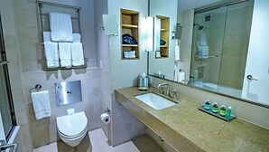 Ein modernes Badezimmer mit Toilette, Waschbecken und Dusche. Handtücher befinden sich an einem Handtuchhalter und über dem Waschbecken hängt ein Spiegel.