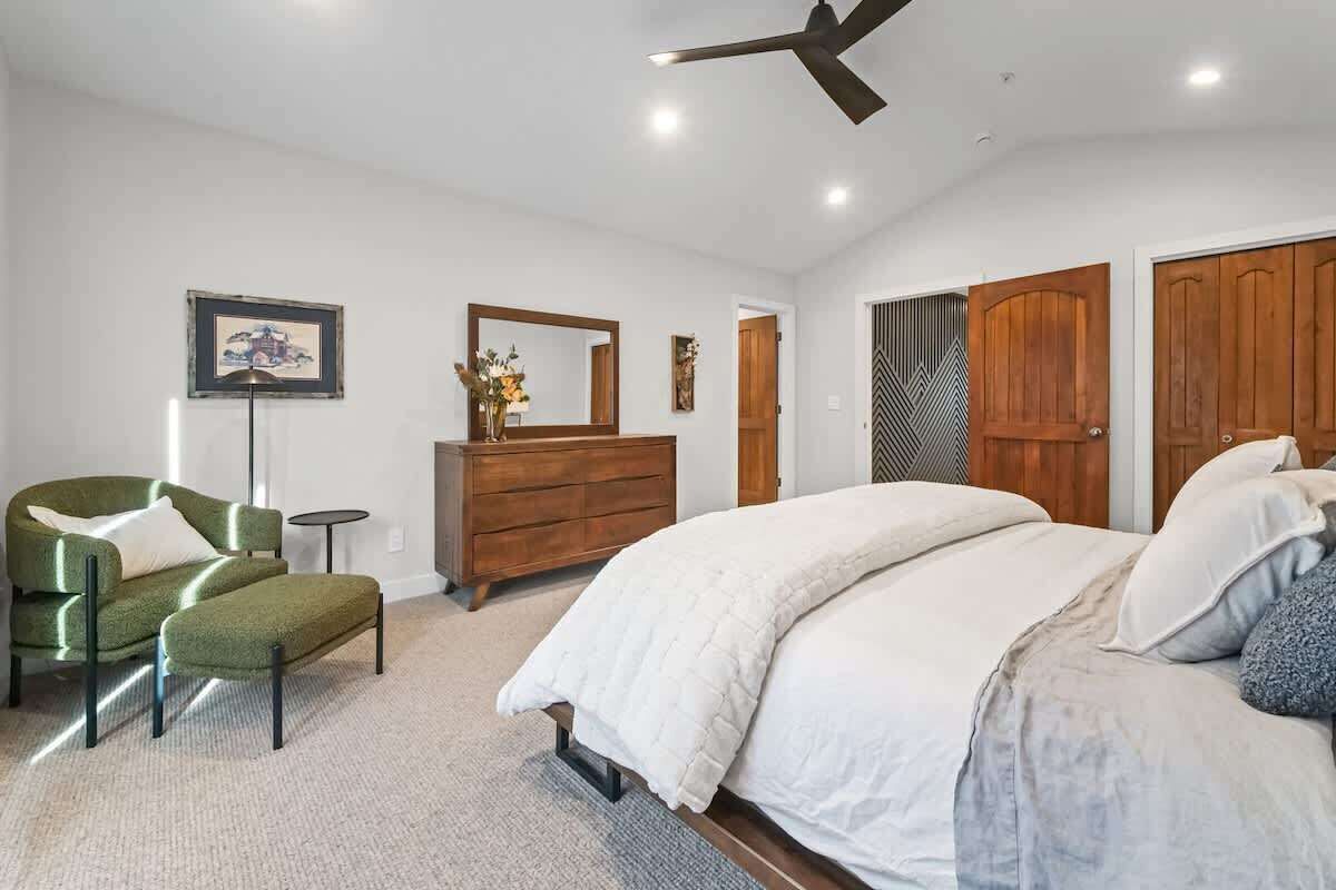 Ein Schlafzimmer mit Bett, Kommode, Stuhl, Spiegel und Deckenventilator.