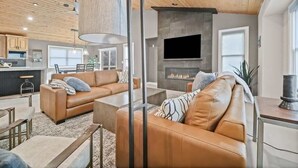 Ein modernes Wohnzimmer mit Ledersofas, einem Kamin und einer Küche im Hintergrund.