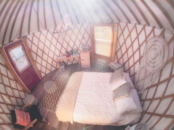 A cozy interior of a yurt with a bed, a small table, and a window.