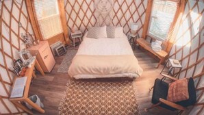 Ein gemütlicher, rundes Jurten-ähnliches Zimmer mit einem Bett, zwei Nachttischen, einem kleinen Tisch und einer Bank.