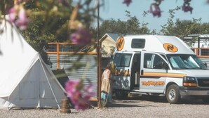 Een witte camper met de aanduiding 'TRAVELLERS' geparkeerd naast een witte tent.