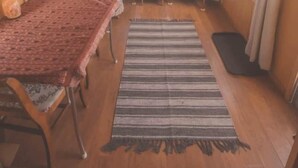 Una habitación compacta con una mesa y sillas de madera, un tapete a rayas y vistas a través de una ventana.