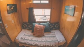 Una habitación pequeña con cama, ventana y una mesita.