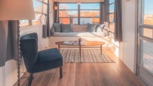 Quarto aconchegante com sofá, poltrona, mesa de centro e janelas amplas com vista para o exterior.