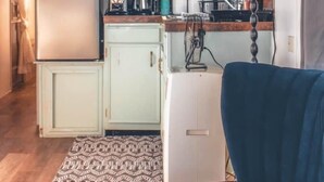 Cozinha compacta com geladeira, micro-ondas e cafeteira. Há um armário pequeno e um tapete estampado no chão.