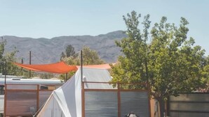 Un camping con una tienda blanca, un toldo rojo y una valla metálica.