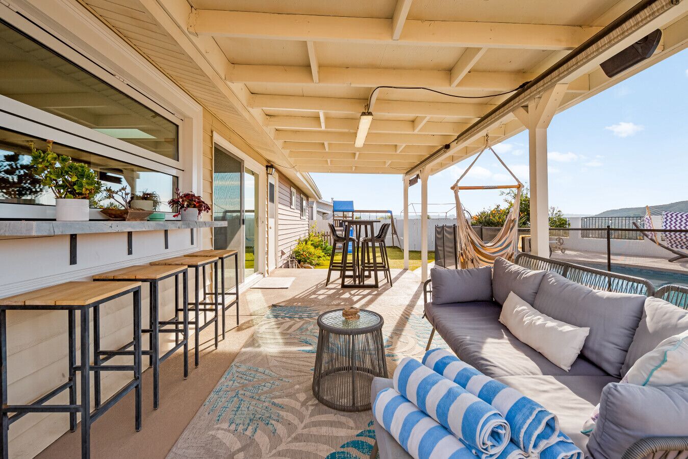 A covered outdoor seating area with a sofa, chairs, and a bar.