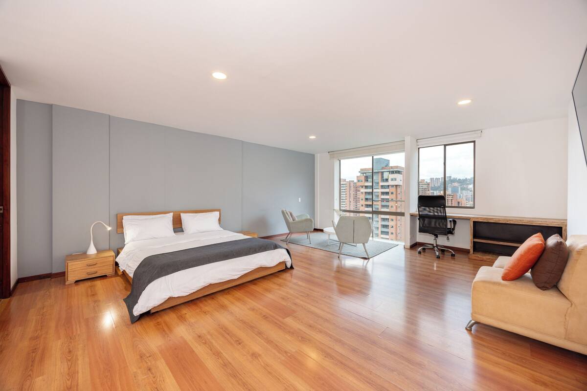 A modern bedroom with a large bed, a desk, and a sofa.
