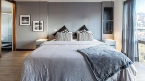 A modern bedroom with a large bed, two bedside tables, and a city view. - Apartamentos SETAI (Medellín)
