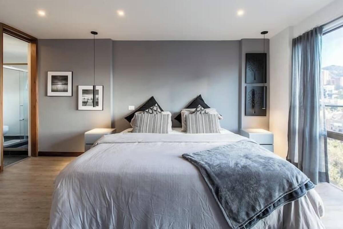 A modern bedroom with a large bed, two bedside tables, and a city view.