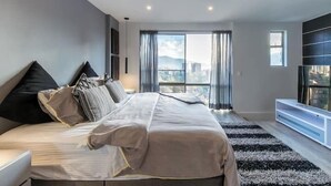 A modern bedroom with a large bed, a TV, and a view of the city. - Apartamentos SETAI (Medellín)
