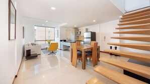 A modern kitchen with a dining area, a staircase, and a living room with a sofa and a yellow chair. - Apartamentos SETAI (Medellín)