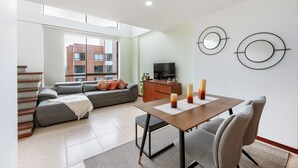 A modern living room with a grey sofa, a dining table with candles, and a TV on a wooden cabinet. - Apartamentos SETAI (Medellín)
